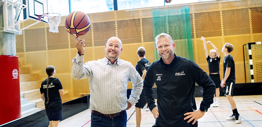 Rektor Johan och idrottsamordnare Jesper Stahre framför elever som spelar basket i bakgrunden. 