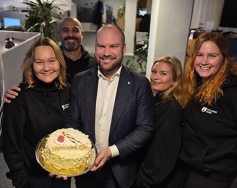 Fem personer står samlade runt en tårta med texten 