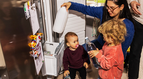 Mamma och två barn framför en frys, som skapar sin hemberedskap genom att frysa in vattenflaskor. 