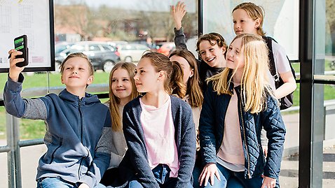 En grupp glada barn i en busskur tar en gruppselfie.