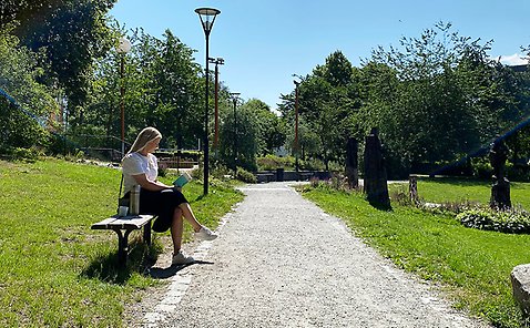 Kvinna sitter på parkbänk vid grusad väg och läser